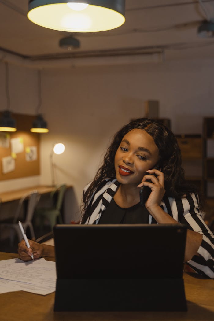 Confident businesswoman multitasking on phone and laptop in a warm office atmosphere.