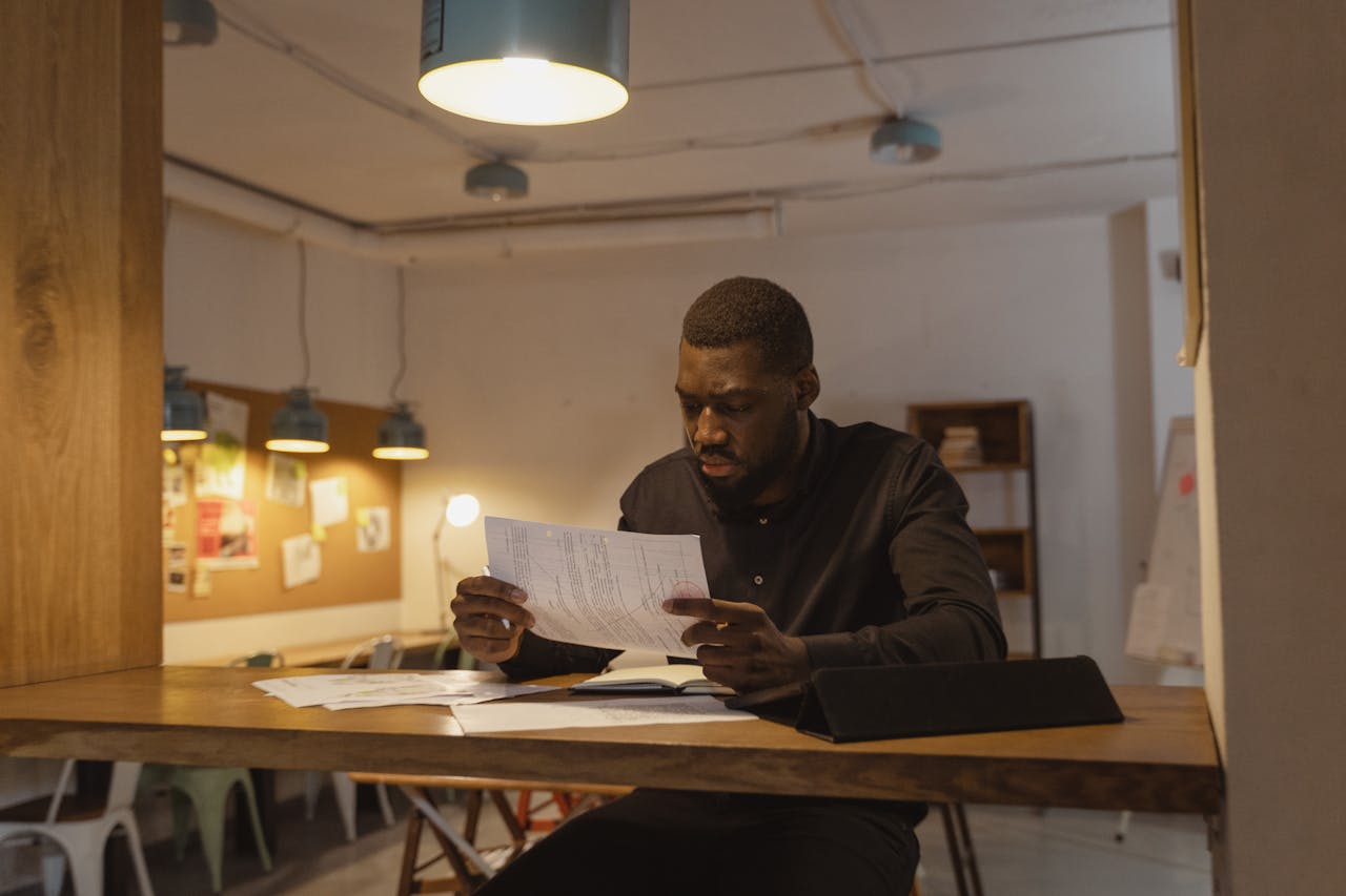 Focused man in office environment analyzing business documents at night.