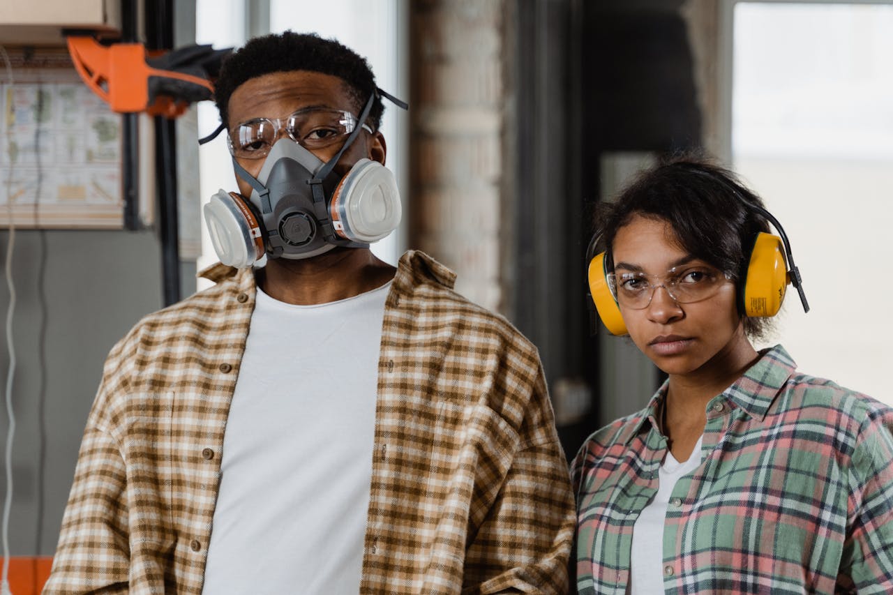Two workers in safety gear stand indoors, highlighting protective equipment in an industrial setting.
